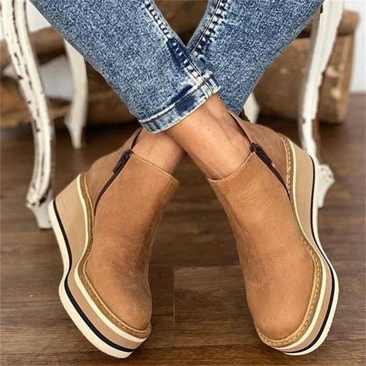 Brown platform shoes worn with blue jeans on a wooden floor