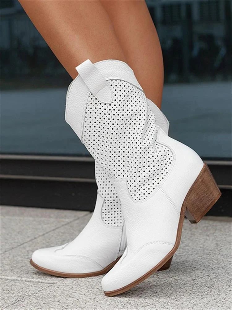 White cowboy boots with brown soles worn by a person on a blurred background